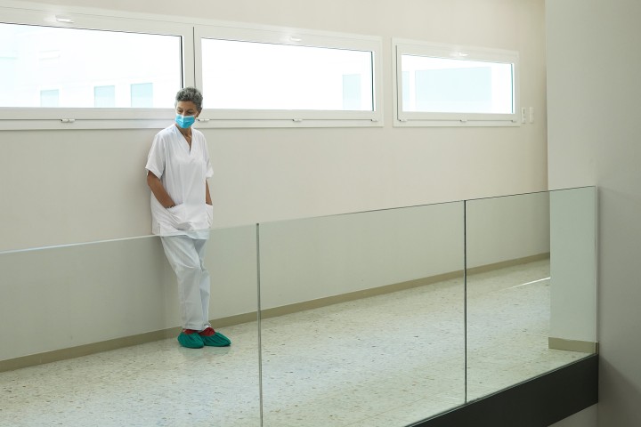 A healthcare worker leans against a wall in an empty corridor