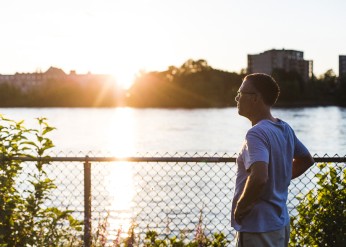 A man looks out onto a river during sunset